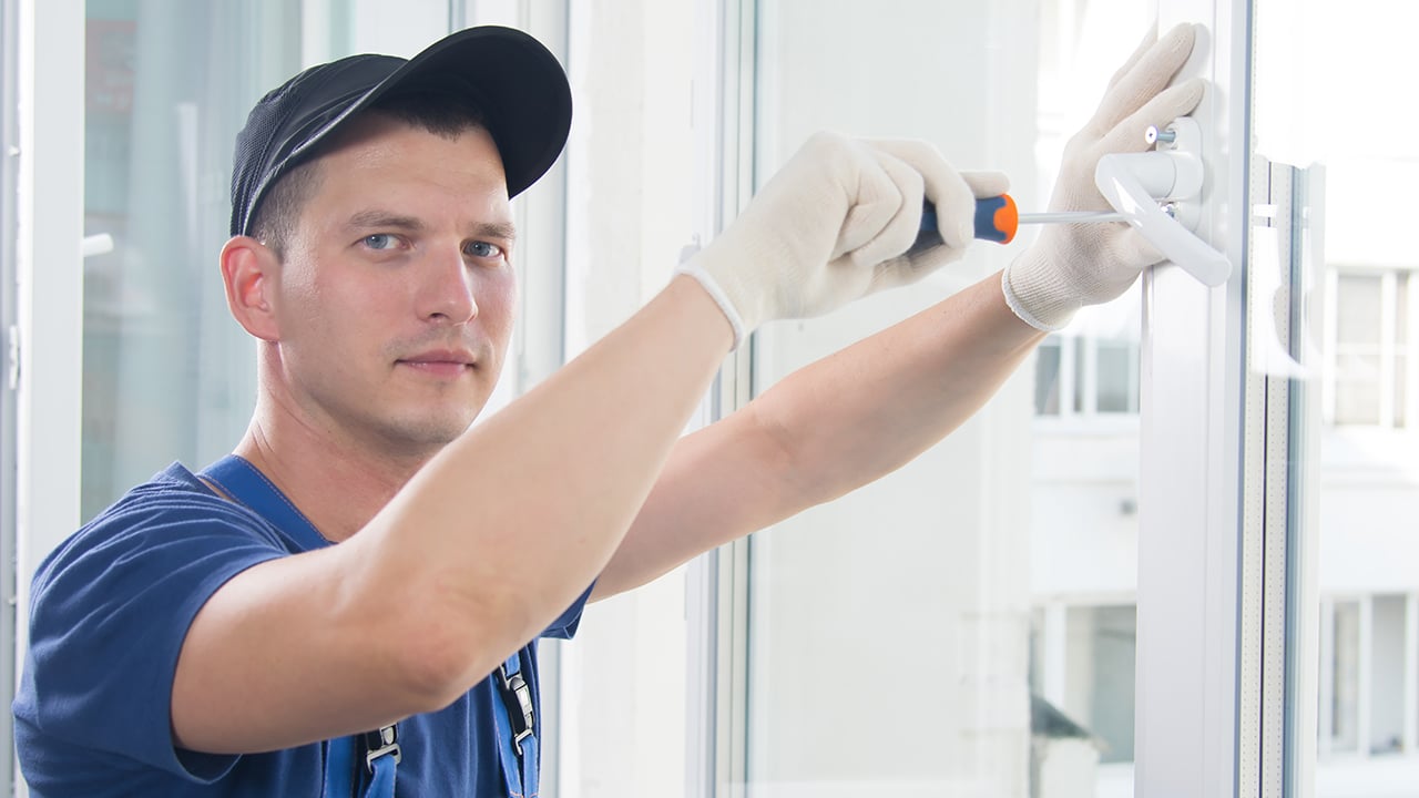 worker in blue uniform screwdriver handles the handle to the plastic window